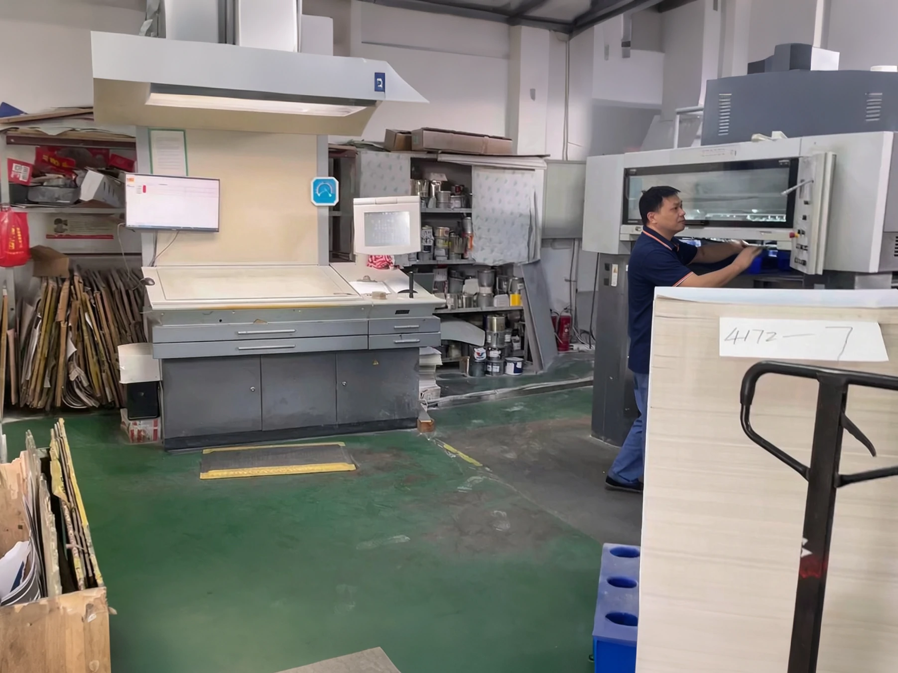An operator running an offset press in the PrintBar workshop, with a paper cutter and stacked board in the foreground An operator running an offset press in the PrintBar workshop, with a paper cutter and stacked board in the foreground